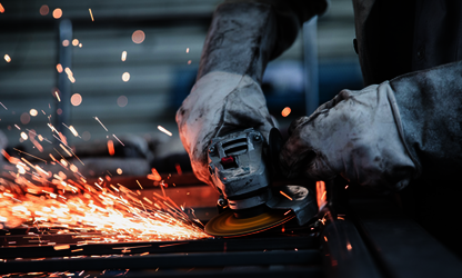 Werden Sie Teil unseres Teams - Zu den aktuellen Stellenangeboten Nahaufnahme eines Handwerkers mit Schutzhandschuhen beim Bearbeiten von Metall mit einem Winkelschleifer und Funkenflug
